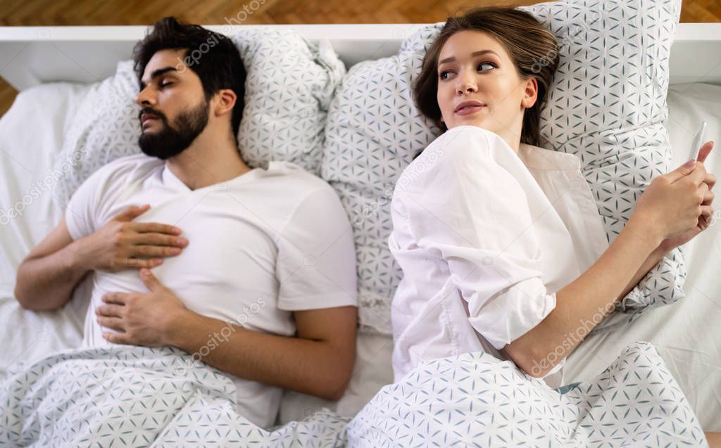 Woman checking her mobile phone while husband sleeping on bed in bedroom