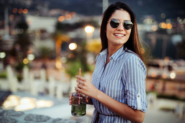 Красивая молодая женщина улыбается и пьет коктейль
