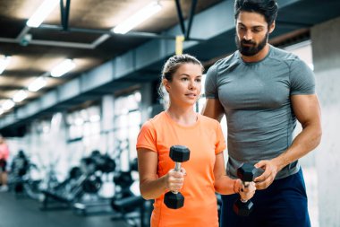 Genç ve güzel bir kadın spor salonunda antrenörle egzersiz yapıyor.