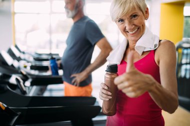 Birlikte spor salonunda koşu bandı üzerinde çalışan mutlu olgun insanlar.