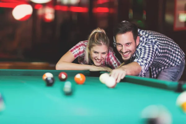 Young couple playing pool in bar while having night out in town