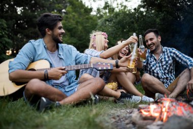 Mutlu arkadaşlar müzik çalıyor ve doğada şenlik ateşinin keyfini çıkarıyorlar.