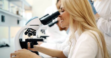 Laboratuvarda mikroskoptan bakan genç kadın bilim adamı.