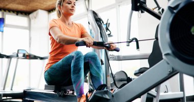 Workout woman cross training exercising cardio using rowing machine in fitness gym clipart