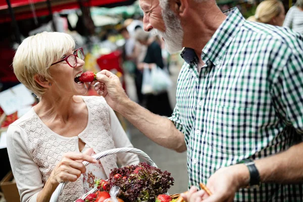 Shopping, food, sale, consumerism and people concept - happy senior couple buying fresh food on the market