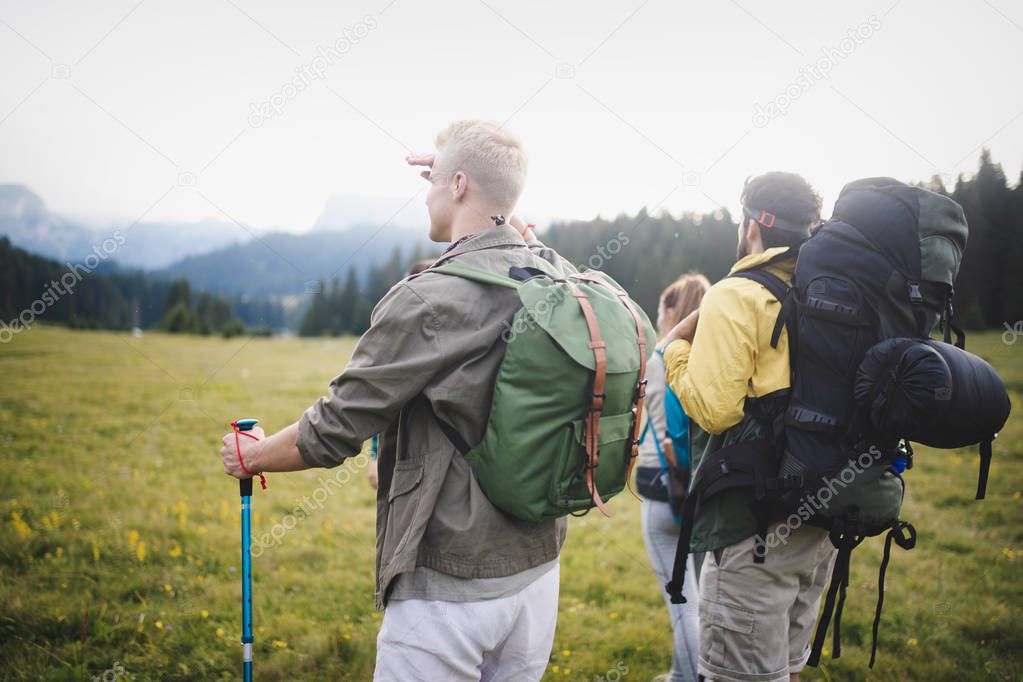 Young gorup of friends climbing up hill, with backpacks and climbing stick