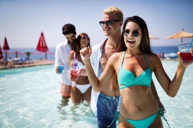 Bir grup mutlu arkadaş havuzda kokteyllerle dans ediyor.