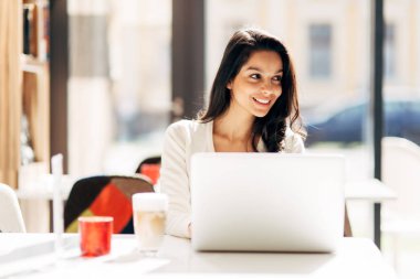 Güzel genç şirin esmer kafede dizüstü bilgisayar kullanarak