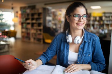 Kütüphanede okuyan üniversiteli kadın mutlu görünüyor. Eğitim kavramları