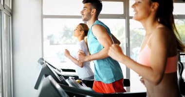 Spor salonunda koşu bandında kardiyo antrenmanı yapan insanların fotoğrafı.