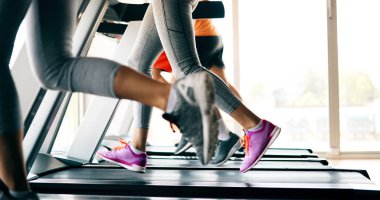 Spor salonunda koşu bandında kardiyo antrenmanı yapan insanların fotoğrafı.