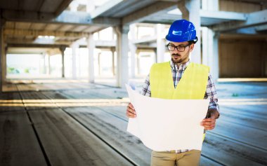 İnşaatta çalışan ve blueprint tutan yakışıklı mühendisi