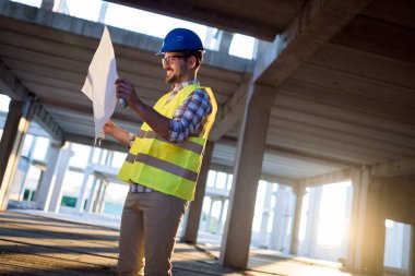 İnşaatta çalışan ve blueprint tutan yakışıklı mühendisi