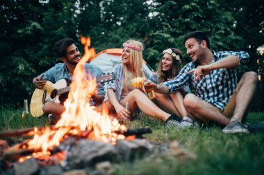 Mutlu arkadaşlar müzik çalıyor ve doğada şenlik ateşinin keyfini çıkarıyorlar.