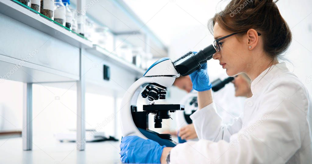 Young female scientist looking through microscope in laboratory