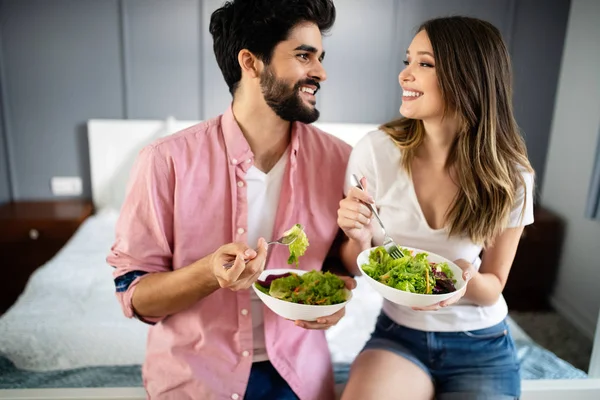 Beautiful young playful couple eating salad together