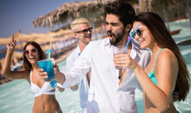 Bir grup mutlu arkadaş havuzda kokteyllerle dans ediyor.