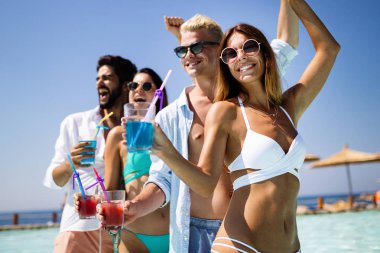 Bir grup mutlu arkadaş havuzda kokteyllerle dans ediyor.