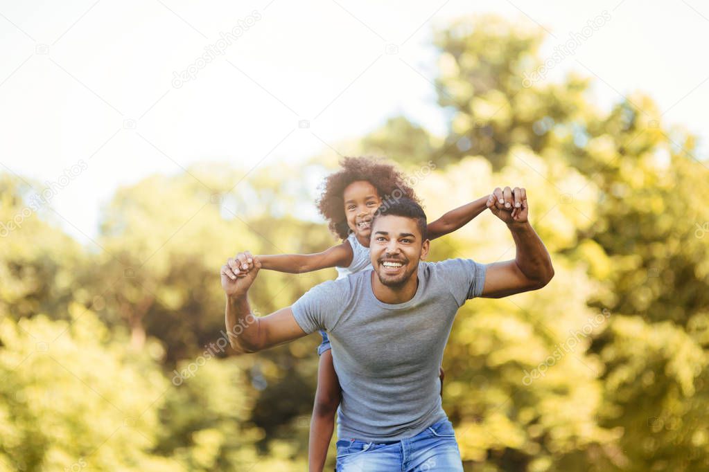 Portrait of young father carrying his daughter on his back in nature