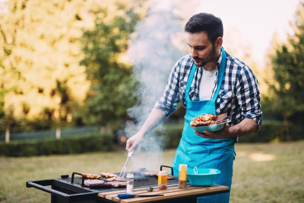 自然の屋外バーベキューの肉を焼く幸せな男性 — ストック写真