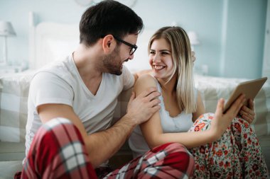 Genç mutlu çift yatak odasında tablet kullanıyor.