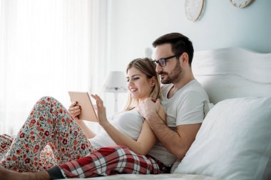 Genç mutlu çift yatak odasında tablet kullanıyor.
