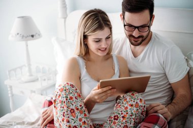 Genç mutlu çift yatak odasında tablet kullanıyor.