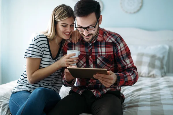 Jong gelukkig paar met behulp van tablet in de slaapkamer — Stockfoto