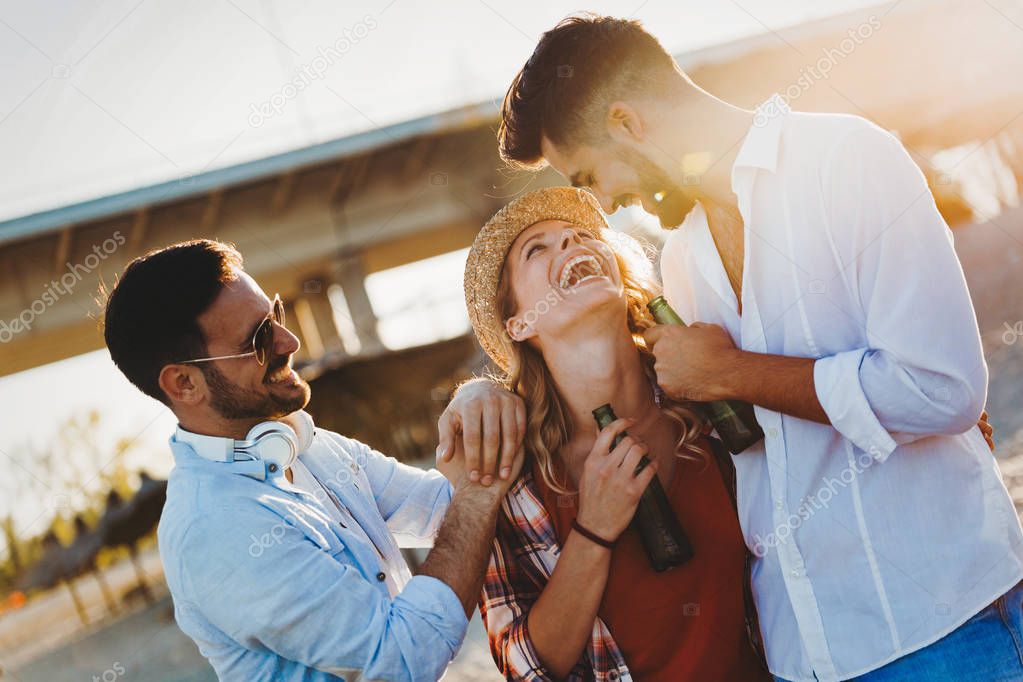 Group of young friends laughing and drinking beer at beach