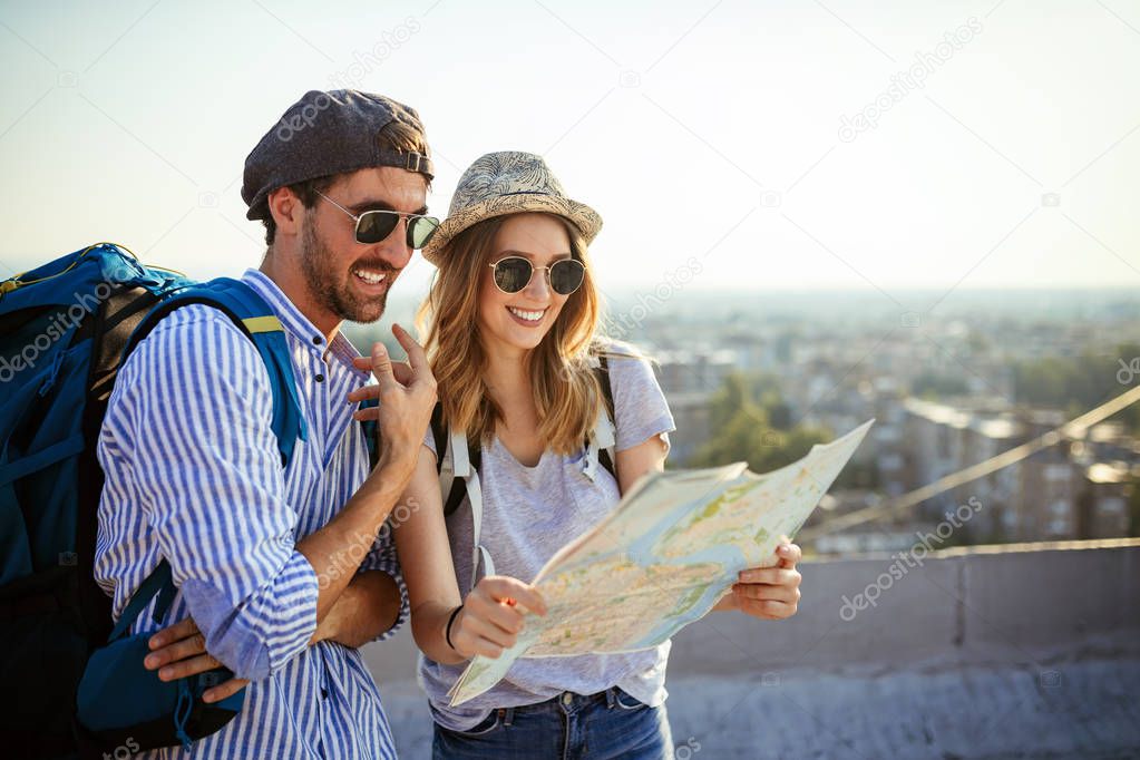 Happy young couple of travellers holding map in hands on vacation