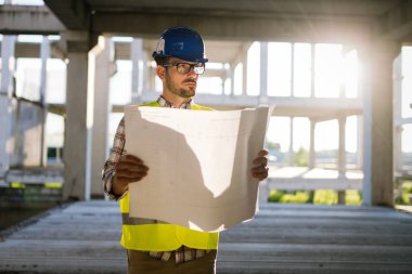 Erkek sitesi yüklenici mühendis baret inşaat alanında mavi baskı kağıdı tutan ile portresi,