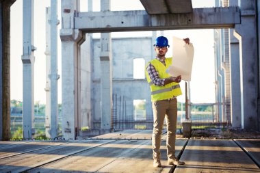 Erkek sitesi yüklenici mühendis baret inşaat alanında mavi baskı kağıdı tutan ile portresi,