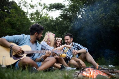 Mutlu arkadaşlar müzik çalıyor ve doğada şenlik ateşinin keyfini çıkarıyorlar.