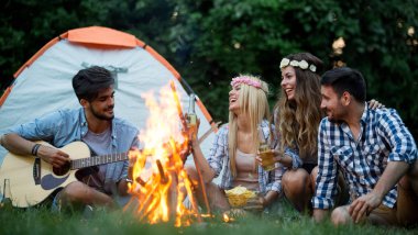 Mutlu arkadaşlar müzik çalıyor ve doğada şenlik ateşinin keyfini çıkarıyorlar.