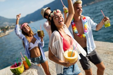 Mutlu arkadaşlar grubu plaj partisinde gün batımında kokteyl içerek eğleniyor. Tatildeki gençlerle yaz neşesi ve arkadaşlık konsepti