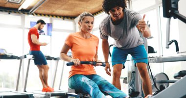 Genç ve güzel bir kadın spor salonunda antrenörle egzersiz yapıyor.