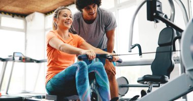 Genç ve güzel bir kadın spor salonunda antrenörle egzersiz yapıyor.