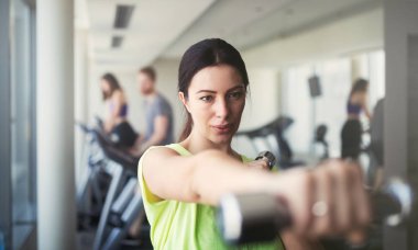 Genç ve güzel bir kadın spor salonunda halterle egzersiz yapıyor. Gülümseyen kızın eğitim sürecinden zevk almasına sevindim.