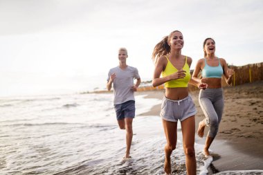 Okyanus cephesinde koşan bir grup sporcu. Spor kıyafetlerinde koşucular açık havada birlikte antrenman yapıyor..