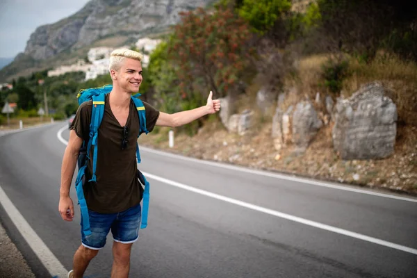 Otostop çeken genç gezgin adam orman yolunda araba yakalamaya çalışıyor. Dünya seyahat yol gezisi, tatil otostop zammı konsepti