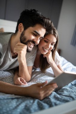 Mutlu çift tablet gibi görünüyor ve yatakta yatarken gülüyorlar.