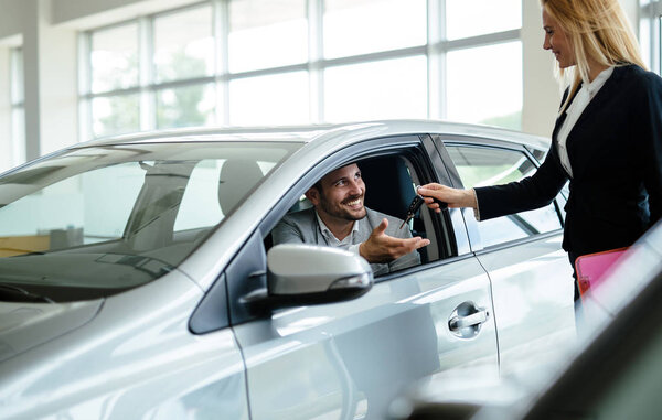 Salesperson during work with customer at car dealership. Giving keys to new car owner.
