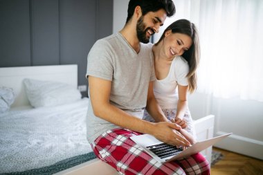 Genç çift yatakta dizüstü bilgisayar ile rahatlatıcı. Aşk, mutluluk, teknoloji, insanlar ve eğlence kavramı.