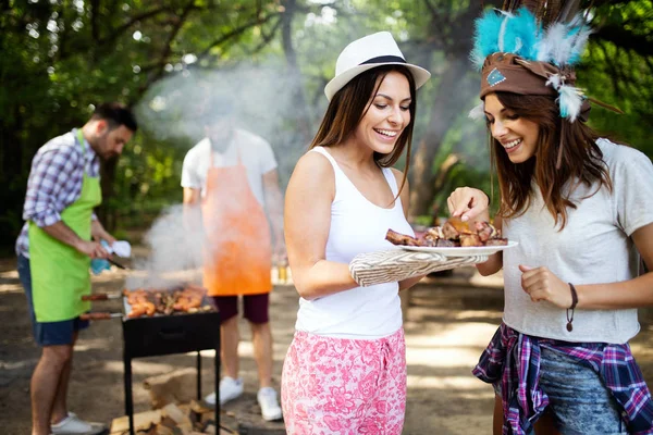 Happy friends making barbecue and having lunch in the nature