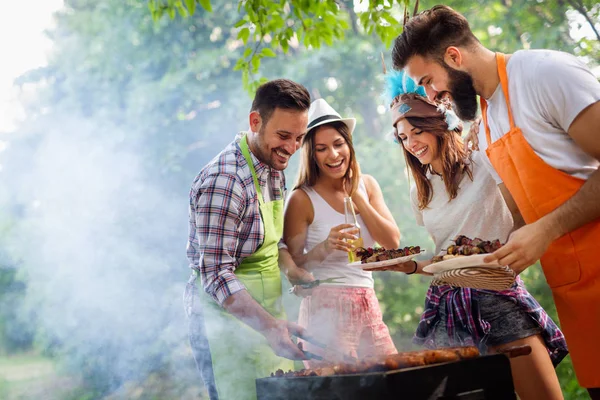 Happy friends making barbecue and having lunch in the nature