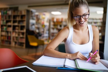 Kütüphanede okuyan üniversiteli kadın mutlu görünüyor. Eğitim kavramları