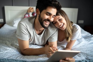 Mutlu çift tablet gibi görünüyor ve yatakta yatarken gülüyorlar.