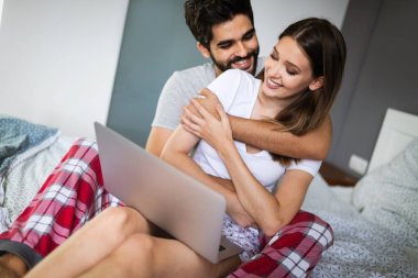 Güzel bir çift yatak odasında birlikte vakit geçirirken gülümsüyor, konuşuyor ve sarılıyor.