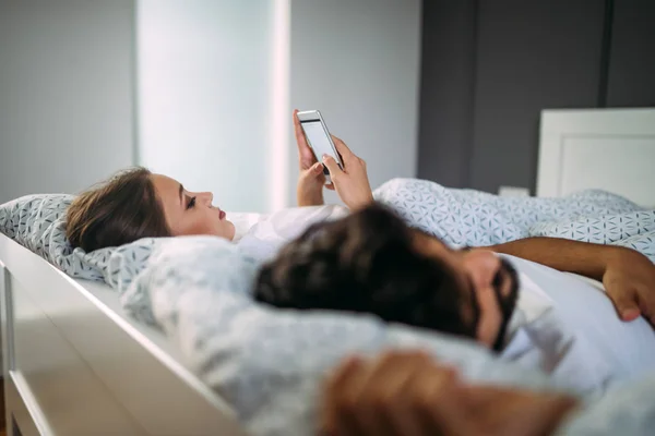Woman texting someone while boyfriend is asleep