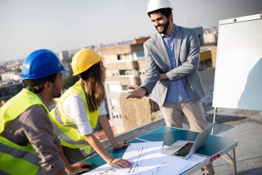 Mimarlar ve mühendislerden oluşan bir ekip inşaat sahasındaki kontrol belgelerini inceleyen gruptakiler.